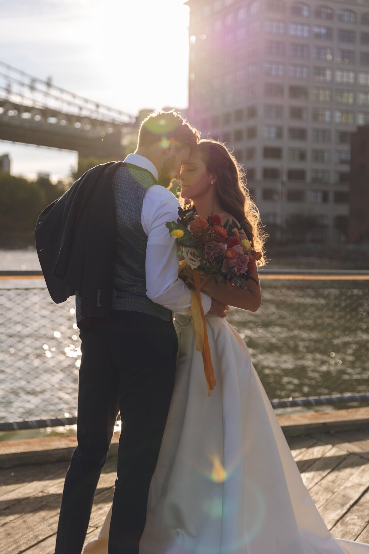 Bride and groom kissing with sun flare over river