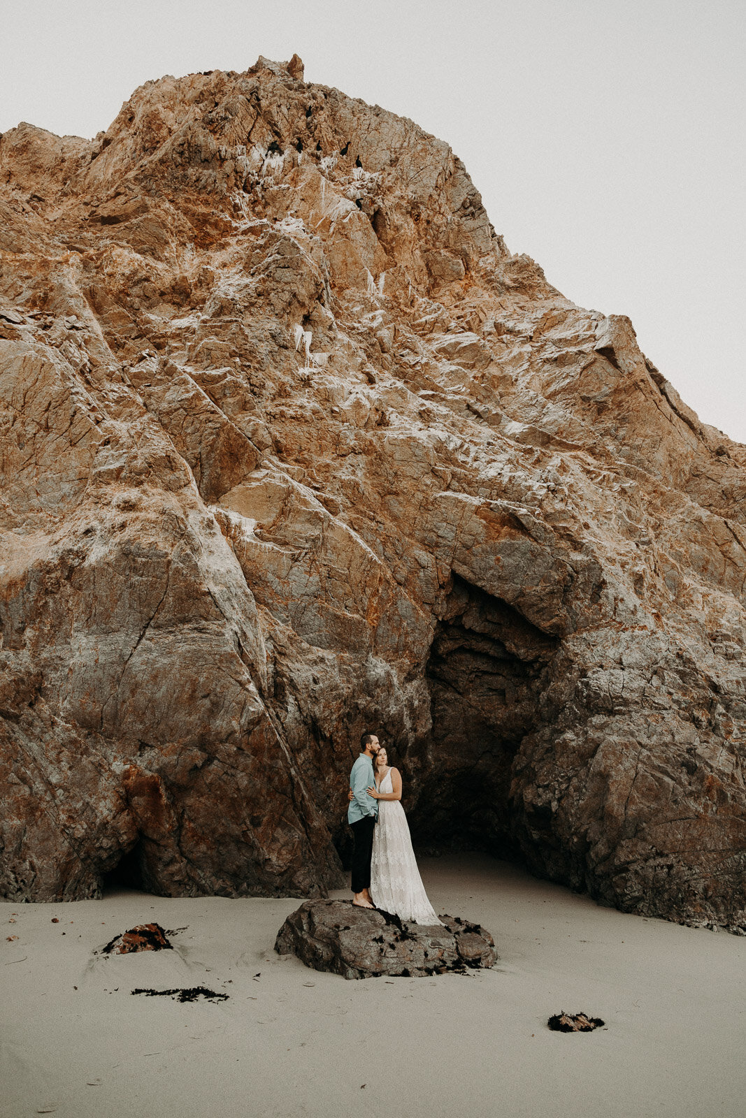 bride and groom kissing on a beach at the foot of a cliff