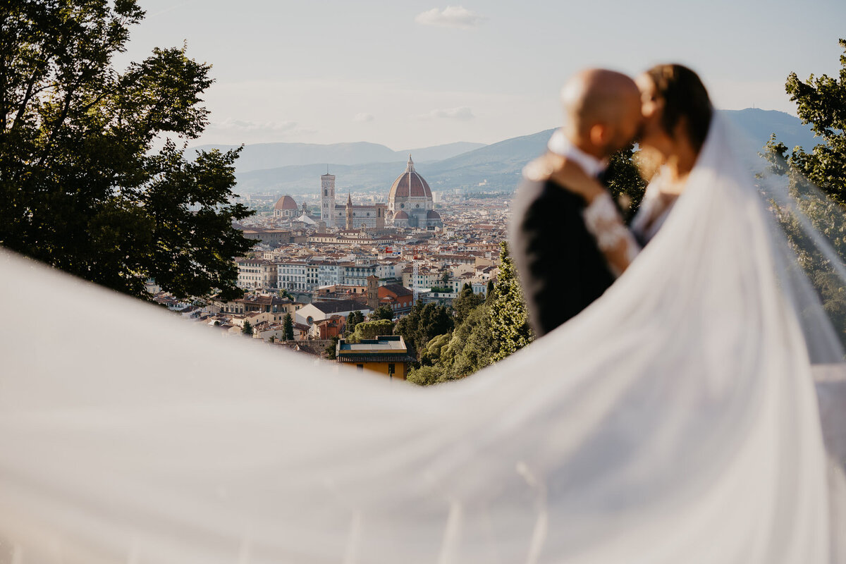Bride and groom kissing with flowing veil and Florence Duomo in background, San Miniato al Monte wedding photographer Tuscany.