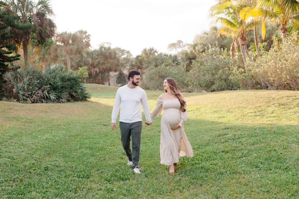 Pregnant couple walking and holding hands in a beautiful green field