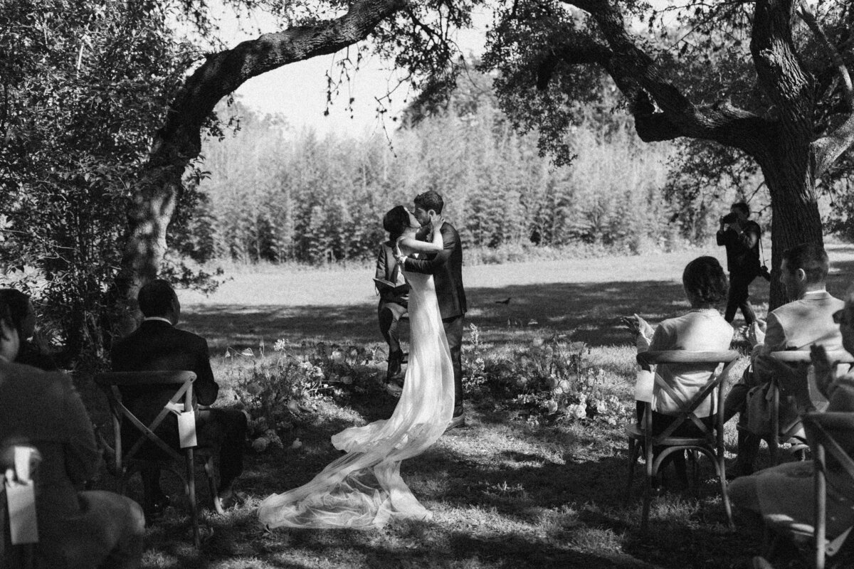 Black and white shot of bride and groom kissing at wedding ceremony under the trees at  Mattie's Austin