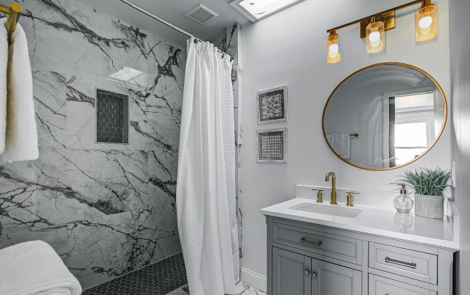 Luxurious bathroom remodel featuring a marble-tiled shower with niche storage, custom vanity with quartz countertop, gold fixtures, and skylight for natural light—designed with elegance and functionality in mind.