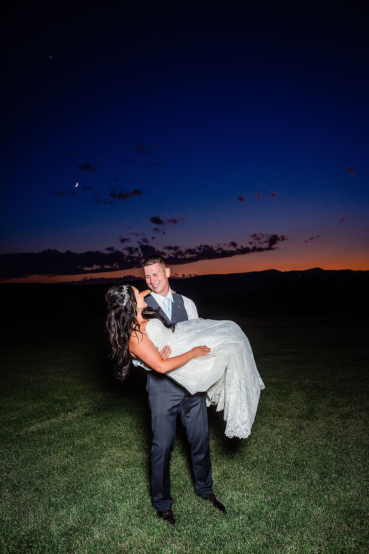 Groom carrying bride through an open grass field with the Montana big sky country sunset behind them