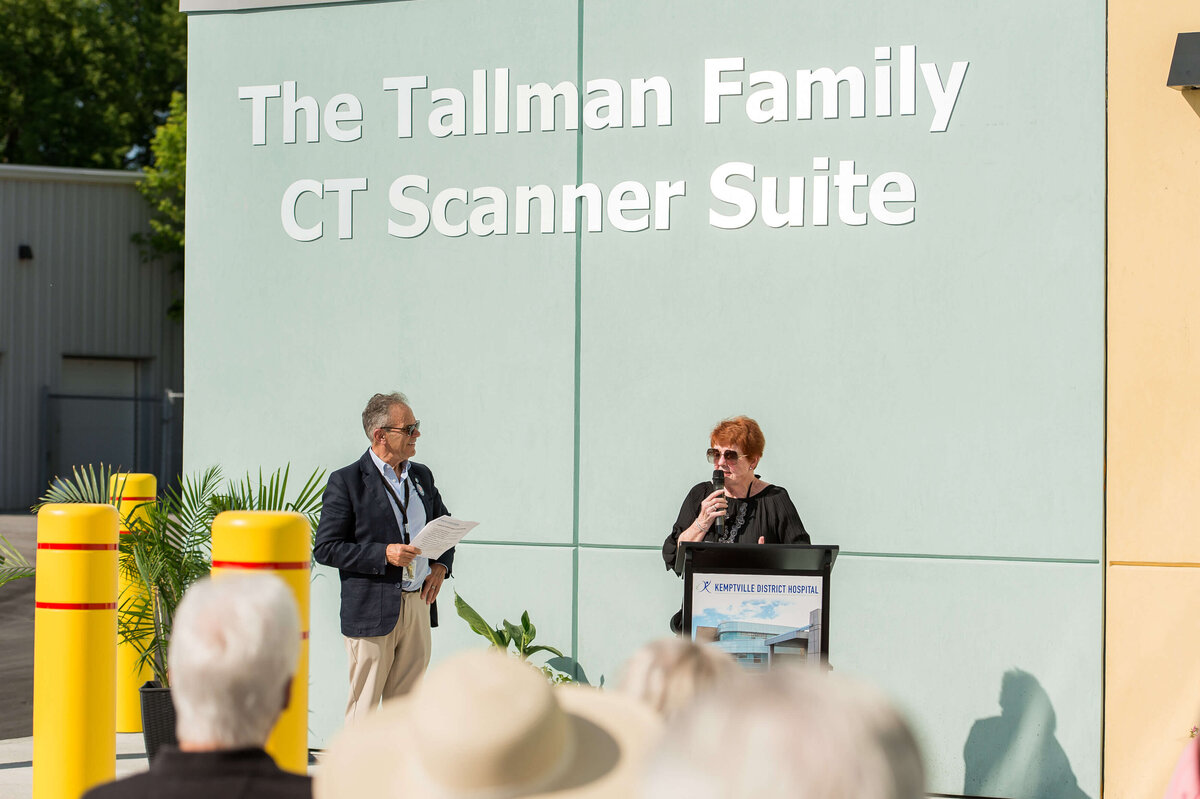 A female donor for the KDH CT Suite speaks into the microphone to address and thank attendees during the grand opening.  Captured by Ottawa Event Photographer JEMMAN Photography COMMERCIAL