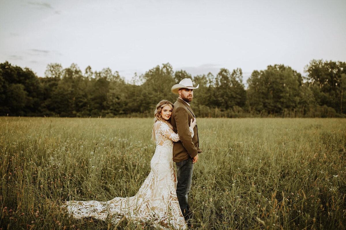 Bride leaning against groom in a field with a relaxed, rustic vibe