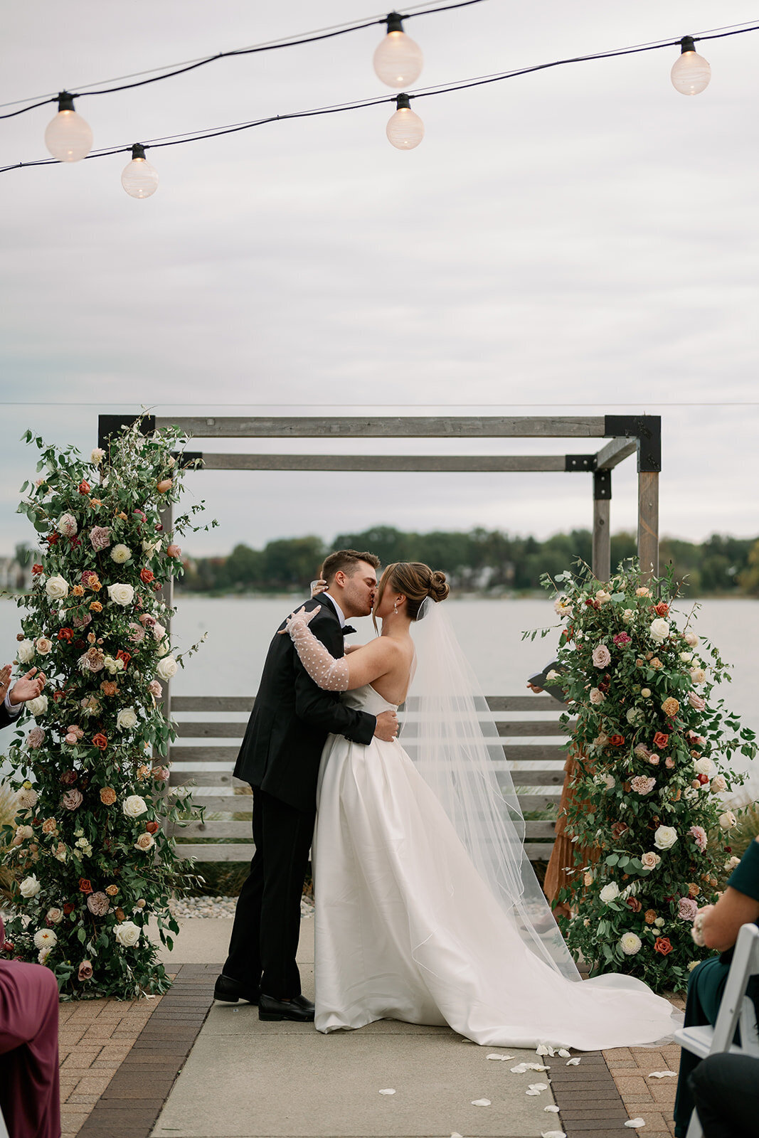 Bride and groom first kiss under floral ceremony arch at Boatwerks Waterfront Venue in Holland Michigan.