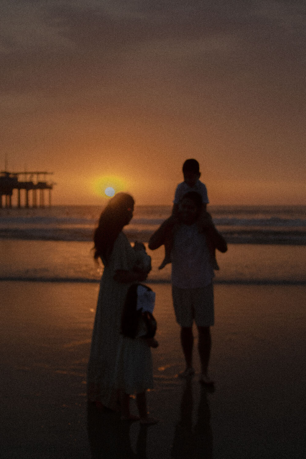 A family silhouetted at sunset on the beach, with the sun low in the sky