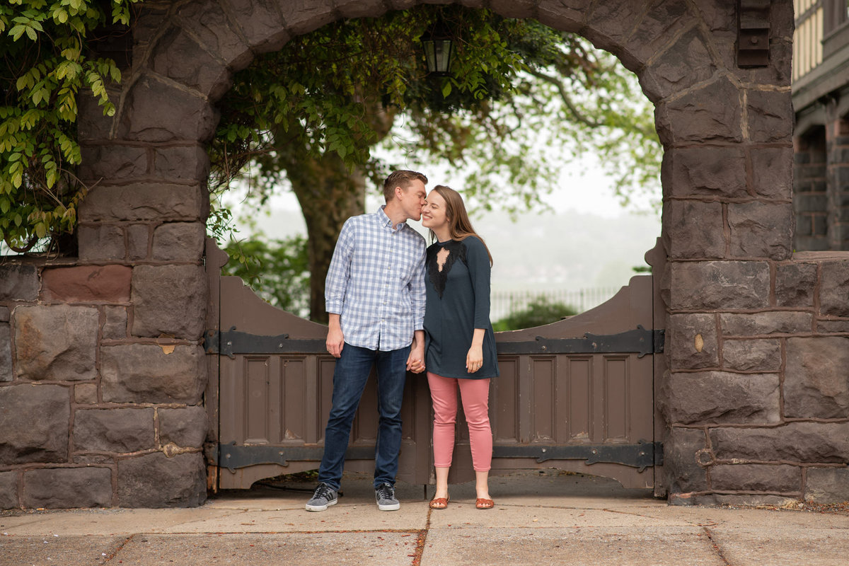 Husband kissing wife's cheek framed in brownstone archway with gate