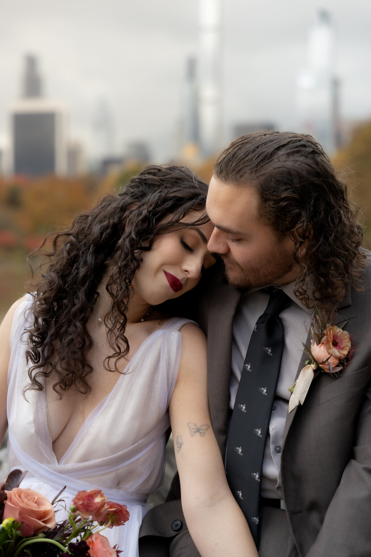 The couple standing close together surrounded by Central Park’s glowing fall foliage.