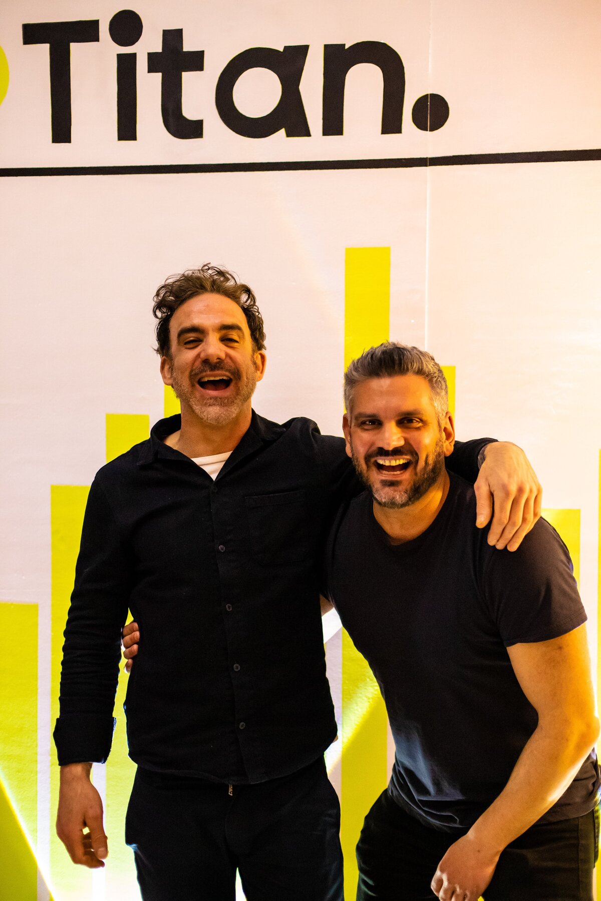 Two smiling men standing together in front of a Titan-branded backdrop.
