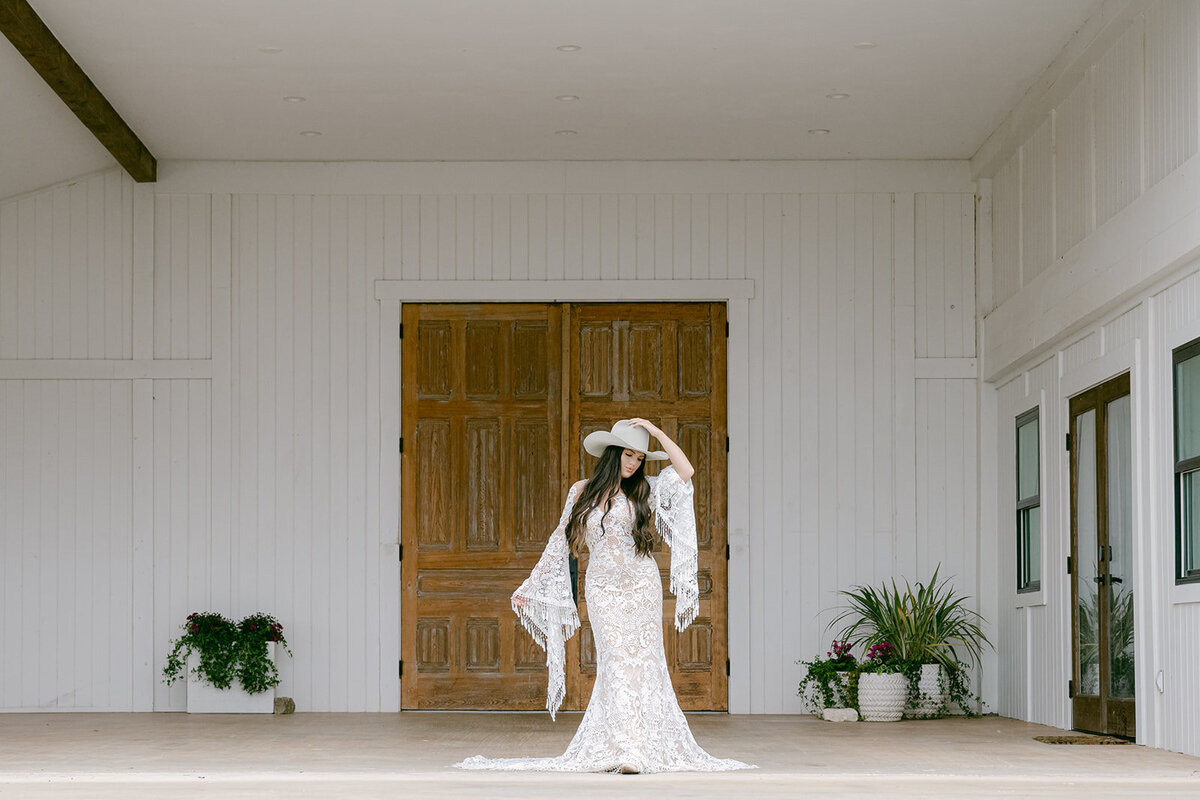 Bridal portrait in lace fringe gown standing in front of wooden doors of the Stables Lodge at The Videre Estate wedding venue.