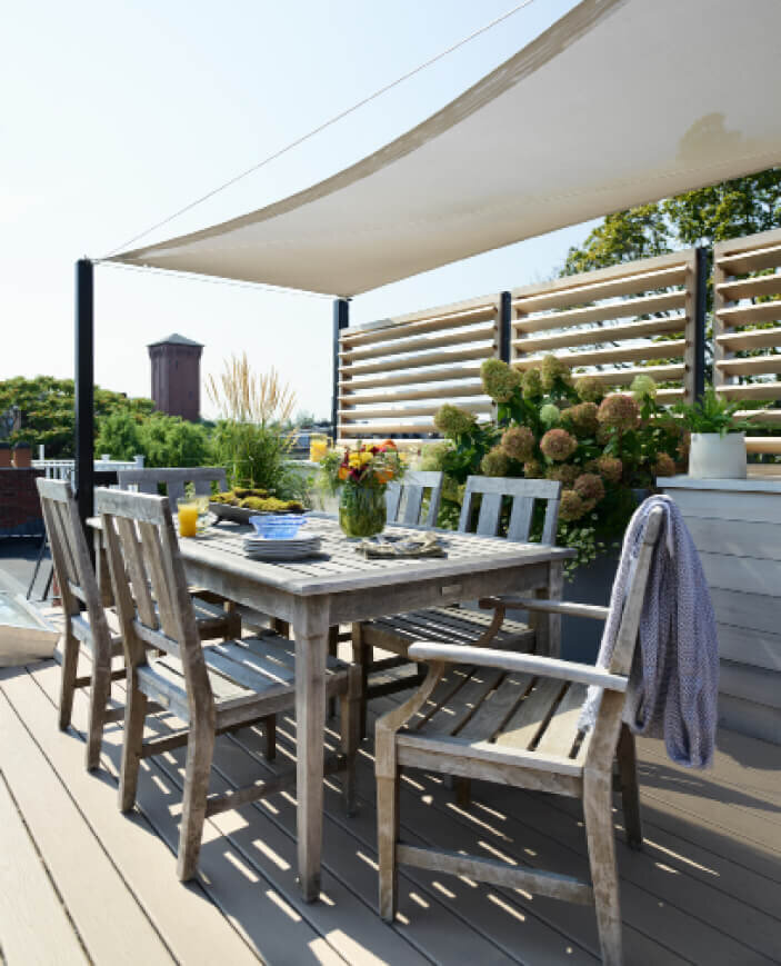 Brownstone Roof Deck Design features outdoor dining furniture, a custom sail cloth shade, and stunning views of the city of Boston.