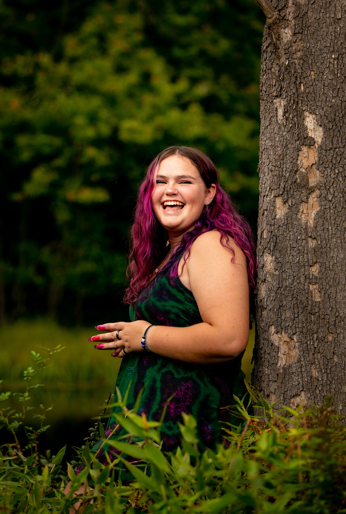 a high school senior clasps her hands in front of her and laughs during a senior photo session
