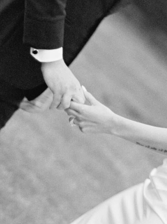 Wedding Photographer RI | A black and white image shows a close-up of two hands gently holding each other. One hand wears a suit, the other a white dress.