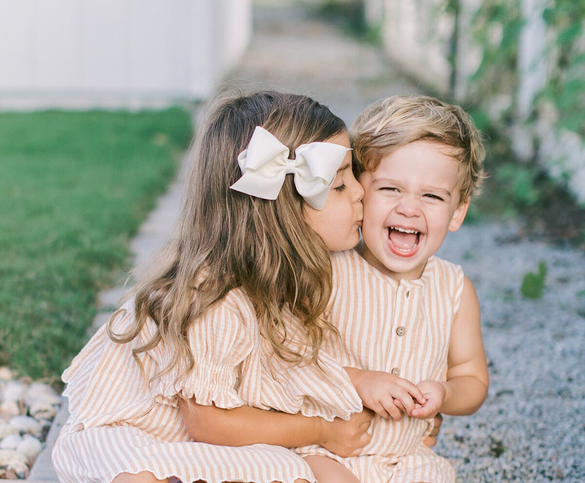A sister kissing her giggling little brother during a playful outdoor session — Raleigh portrait photographer.