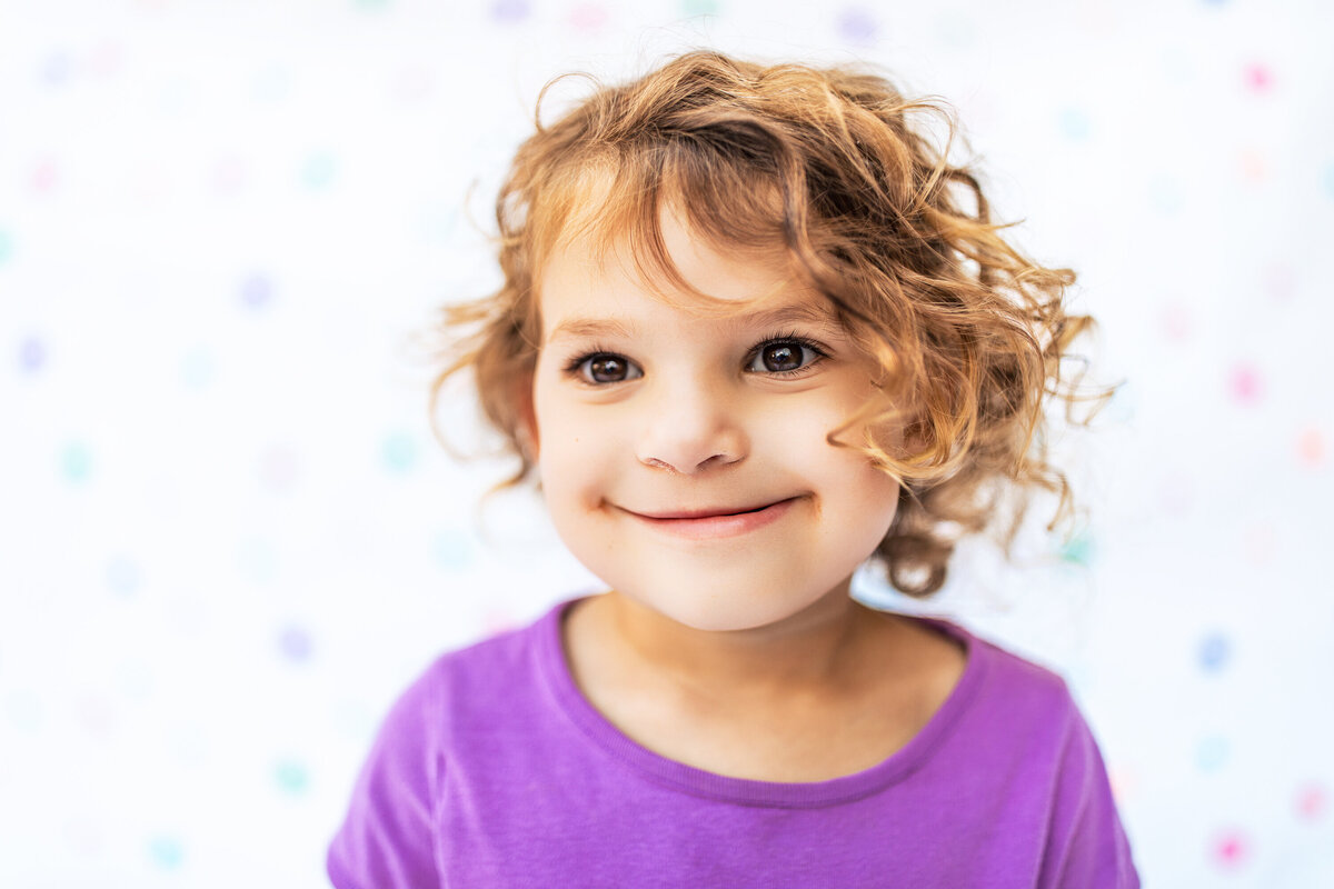 A girl wearing a bright purple top with beautiful brown curls and brown eyes poses for a portrait near Sewickley Pennsylvania for photographer Heidi iliff