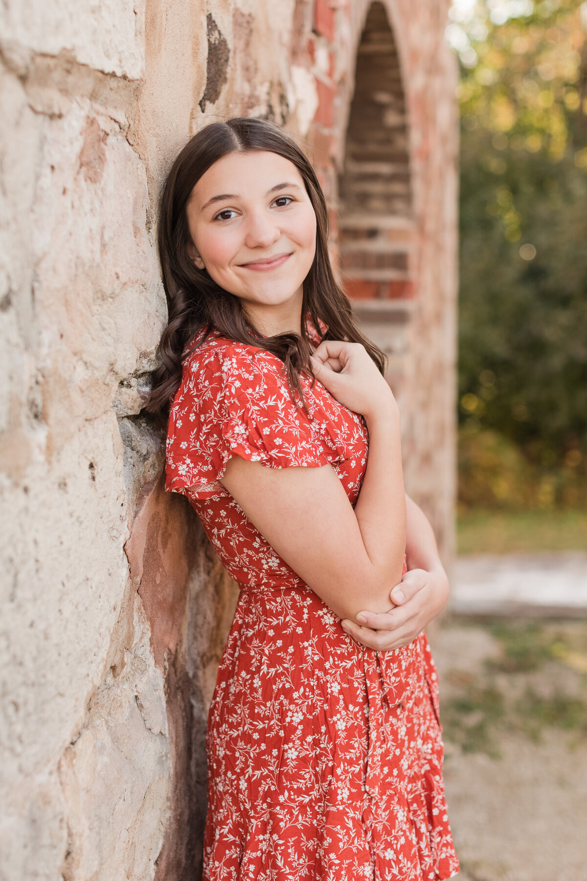 Senior girl leaning against a wall smiling at the camera