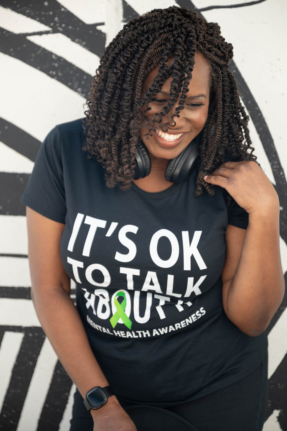 a portrait of a woman wearing a black t-shirt and headphones smiling looking down to the floor