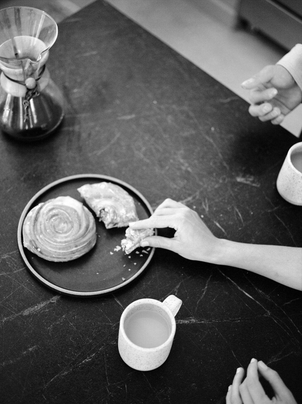 hands reach over dark countertop for cinnamon rolls, coffee, lifestyle interior brand photography on film in Michigan