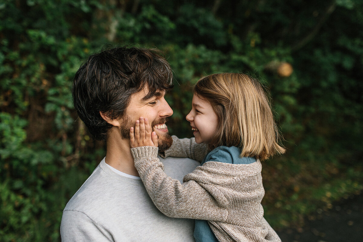 A young girl holder daddys face while they smile at each other as he holds her.