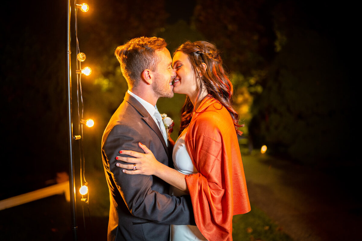 wedding photo showing bride and groom sharing a kiss next to string lights in the gardens of Phipps conservatory
