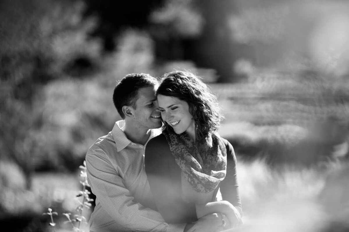 Couple seated together in nature, with a gentle smile and soft light creating a dreamy atmosphere.
