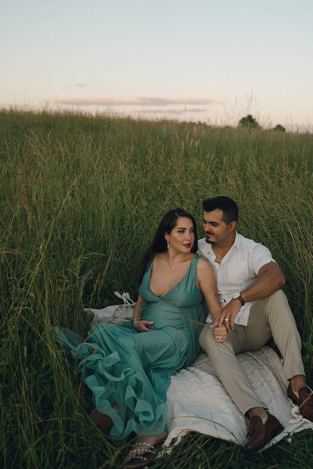 Pregnant woman sitting in tall grass with her partner, captured during a golden-hour maternity session in Northern Virginia