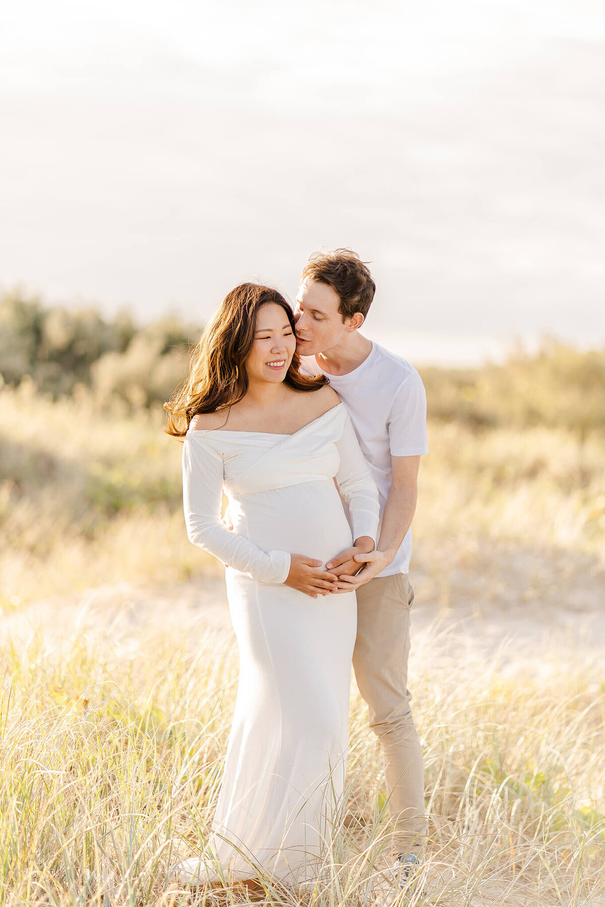 Man whispering in woman's ear making her laugh during maternity photoshoot in Gold Coast