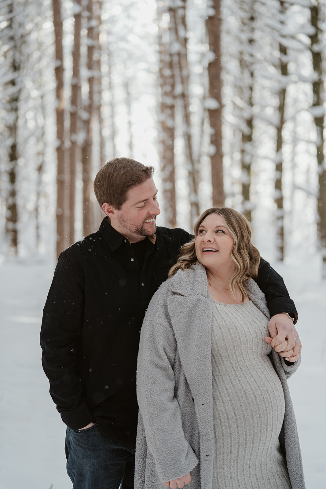 Pregnant couple walking together through a snow-covered trail at Al Sabo Preserve during their Michigan maternity photography session.