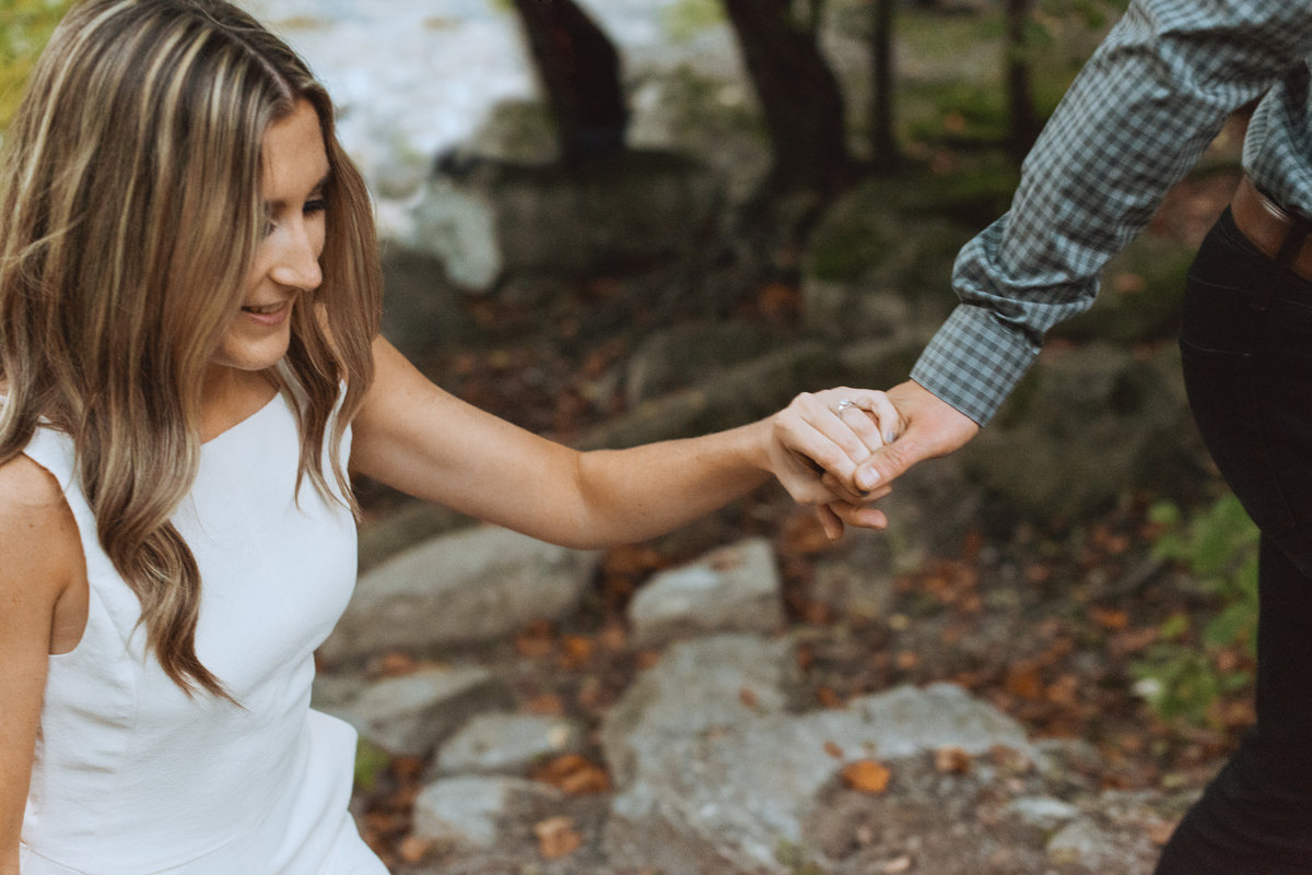 engaged girl holding her fiancee's hand in the woods