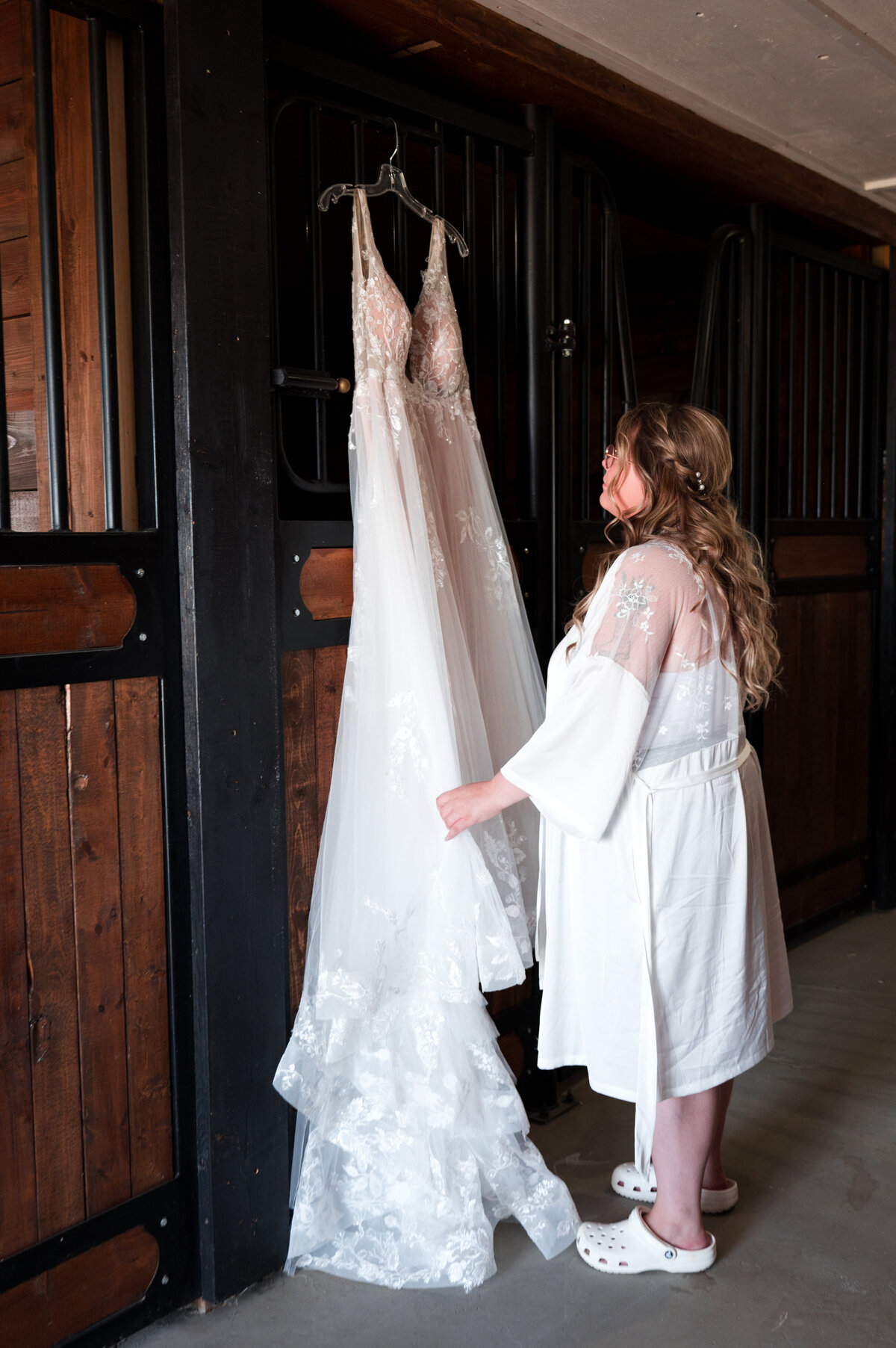 bride holding onto wedding dress hanging in horse stable 