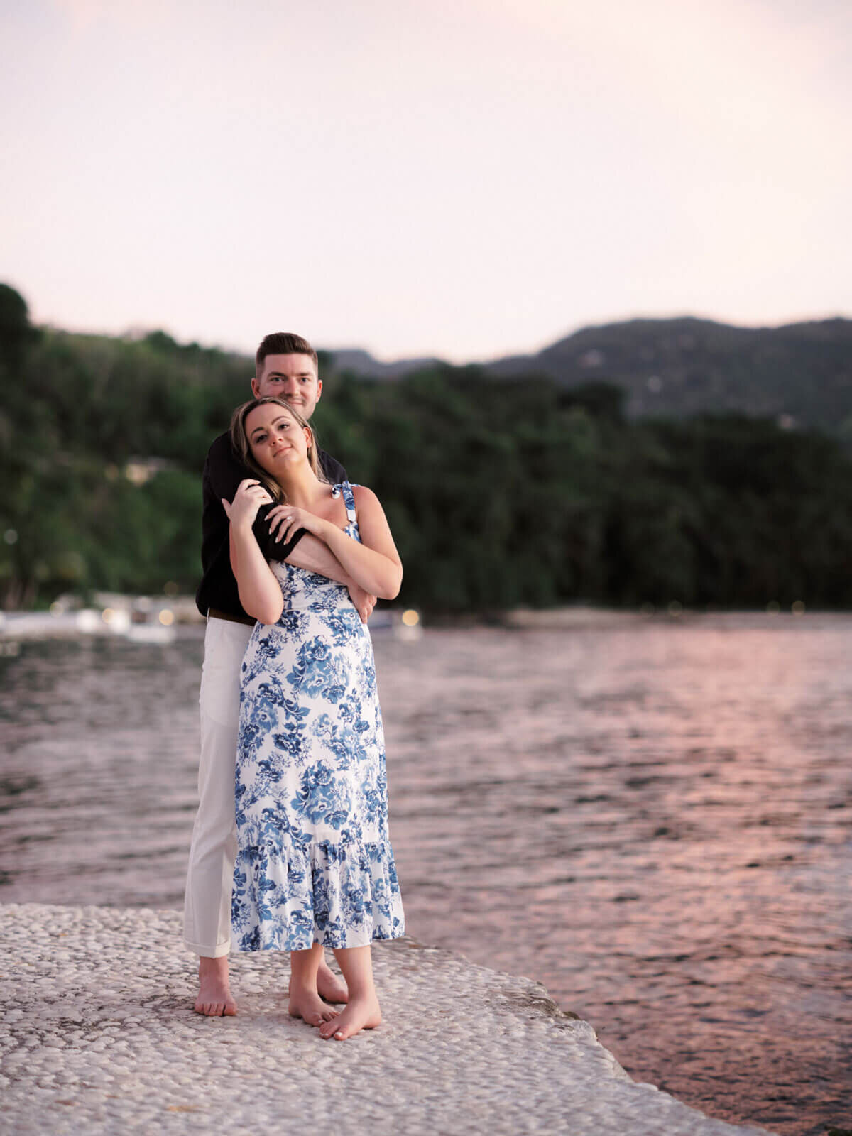 The engaged couple is standing on cobblestone ground at Roundhill Hotel and Villas, Jamaica, with the ocean on the background.
