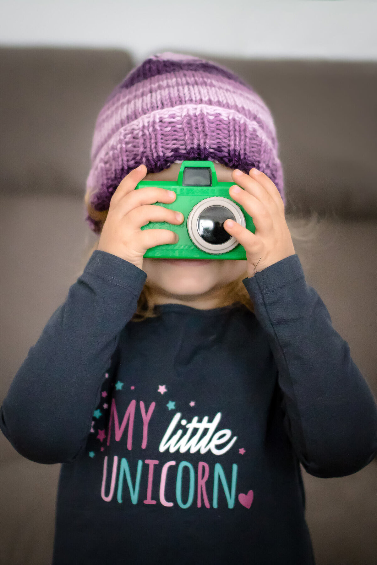 My daughter holding a little green toy camera up to her face and taking a picture of me taking a picture of her.