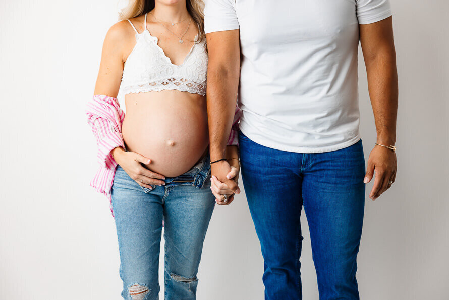 A pregnant couple hold hands.