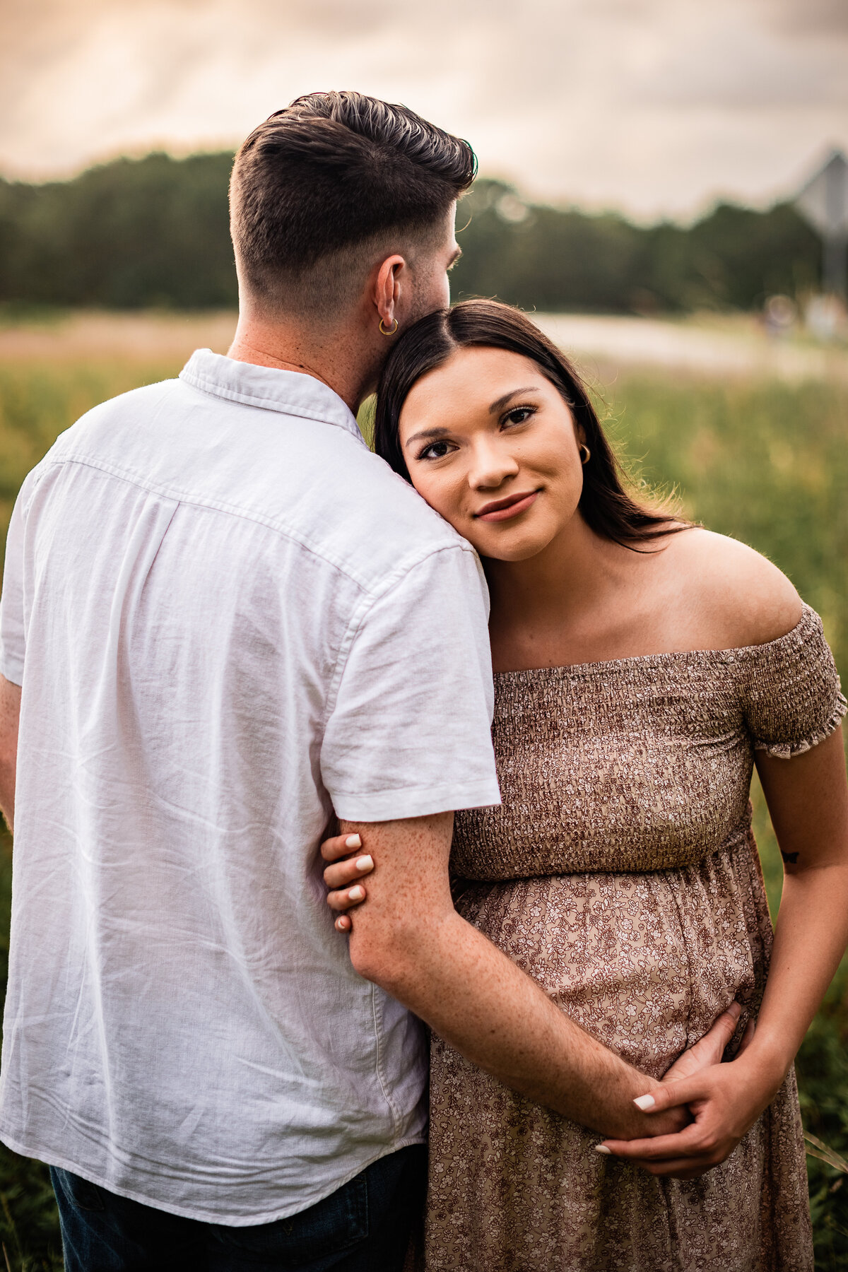 A mom to be leans her head on her boyfriend's shoulder as he holds her belly bump.