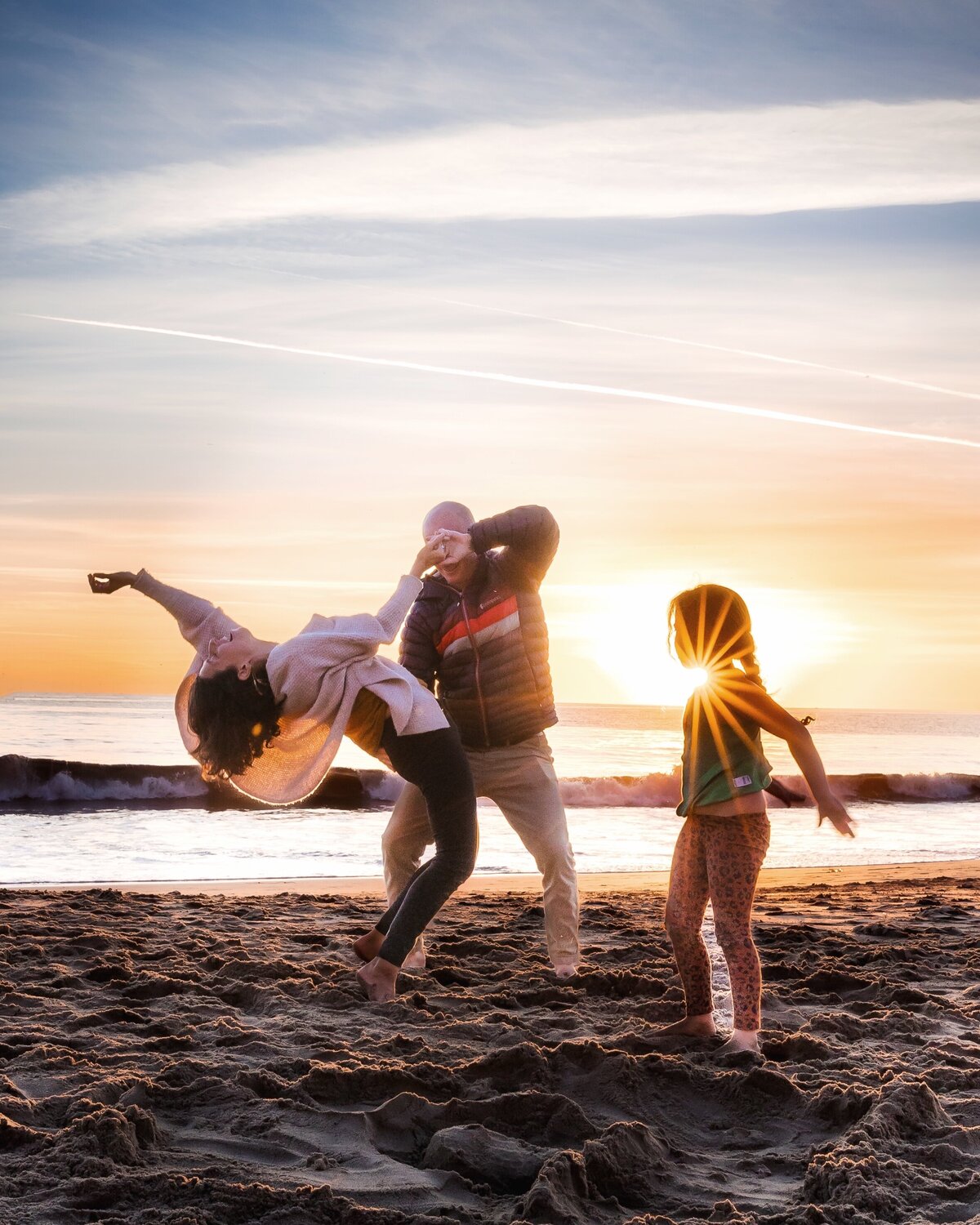 Family dances on the beach at sunset with sunburst