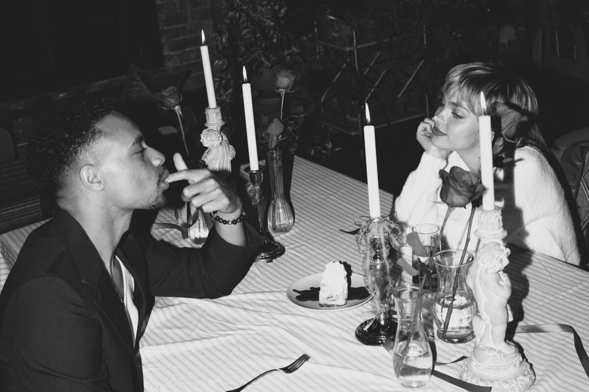 A bride and groom are sitting at an elegant table, looking at each other.