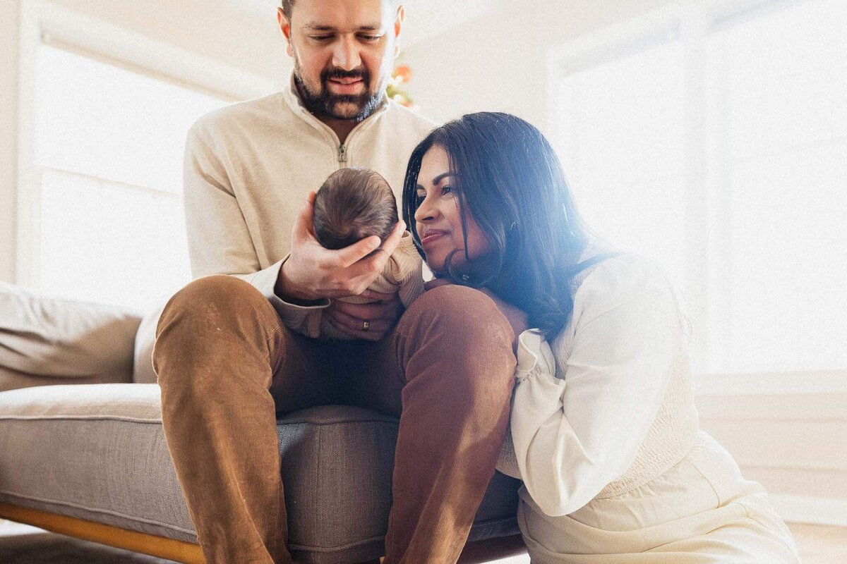 Mom and dad admiring their newborn on modern couch during newborn photography session in Cleveland.