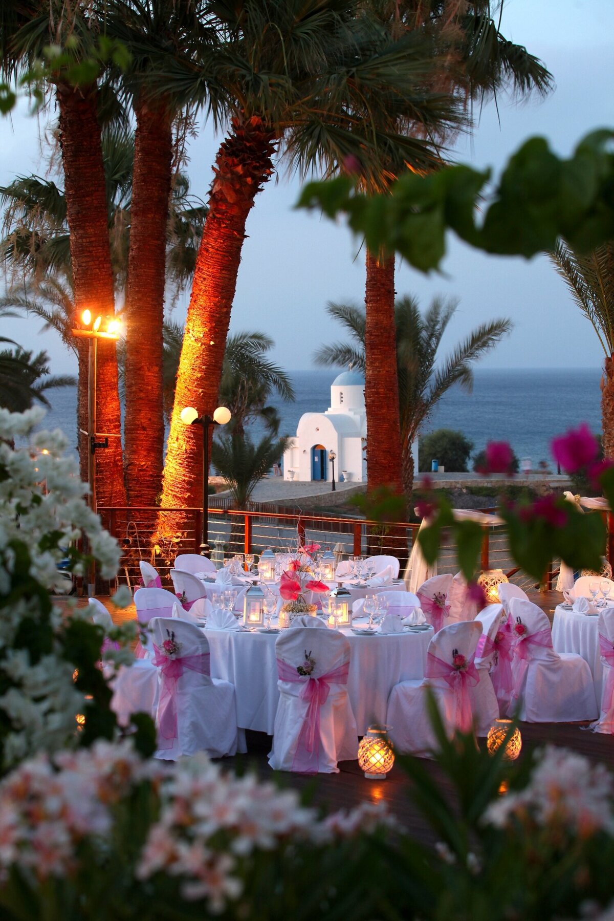 Banqueting tables decorated with pink voile sit infront of a backdrop of a quaint chapel in the distance