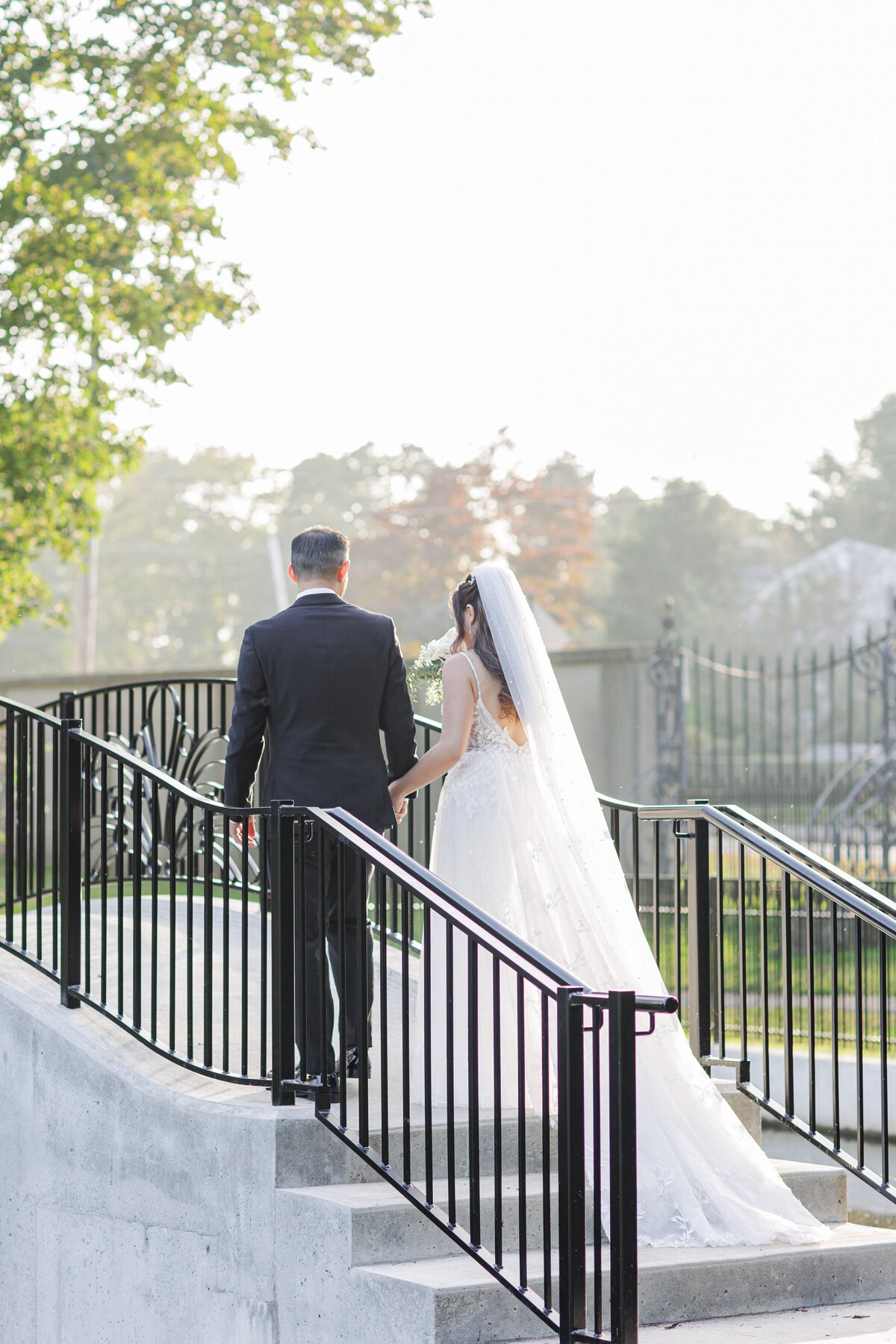 Bride and groom holding hands and walking over a bridge at Larz Anderson  Park