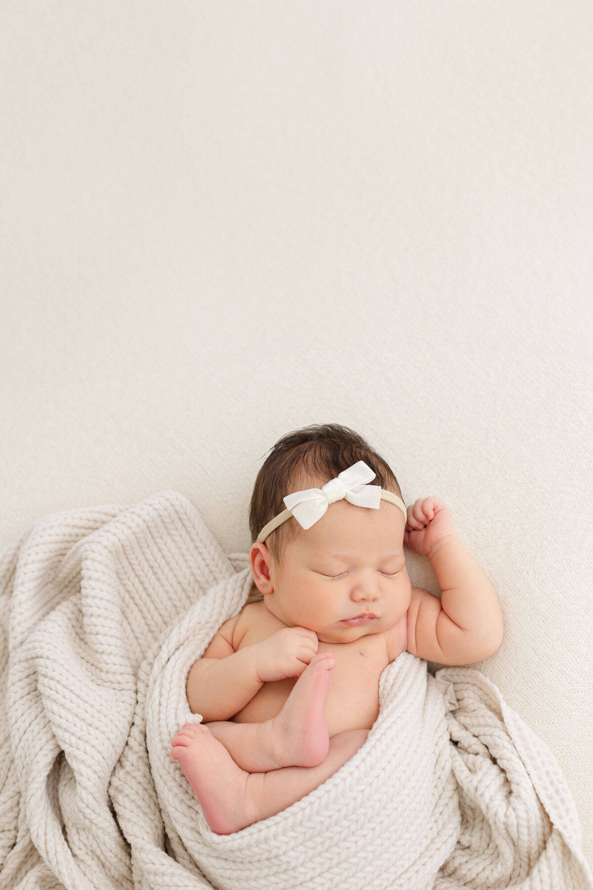 Newborn baby photo on beige backdrop with lots of negative space above baby's head. Artsy newborn photos