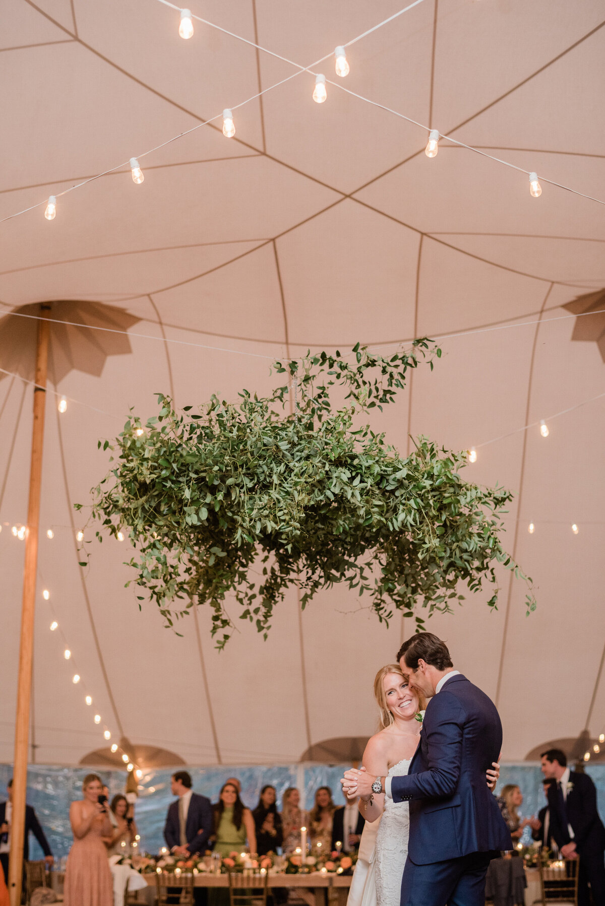 The newlyweds share a romantic first dance under a greenery installation inside a tent