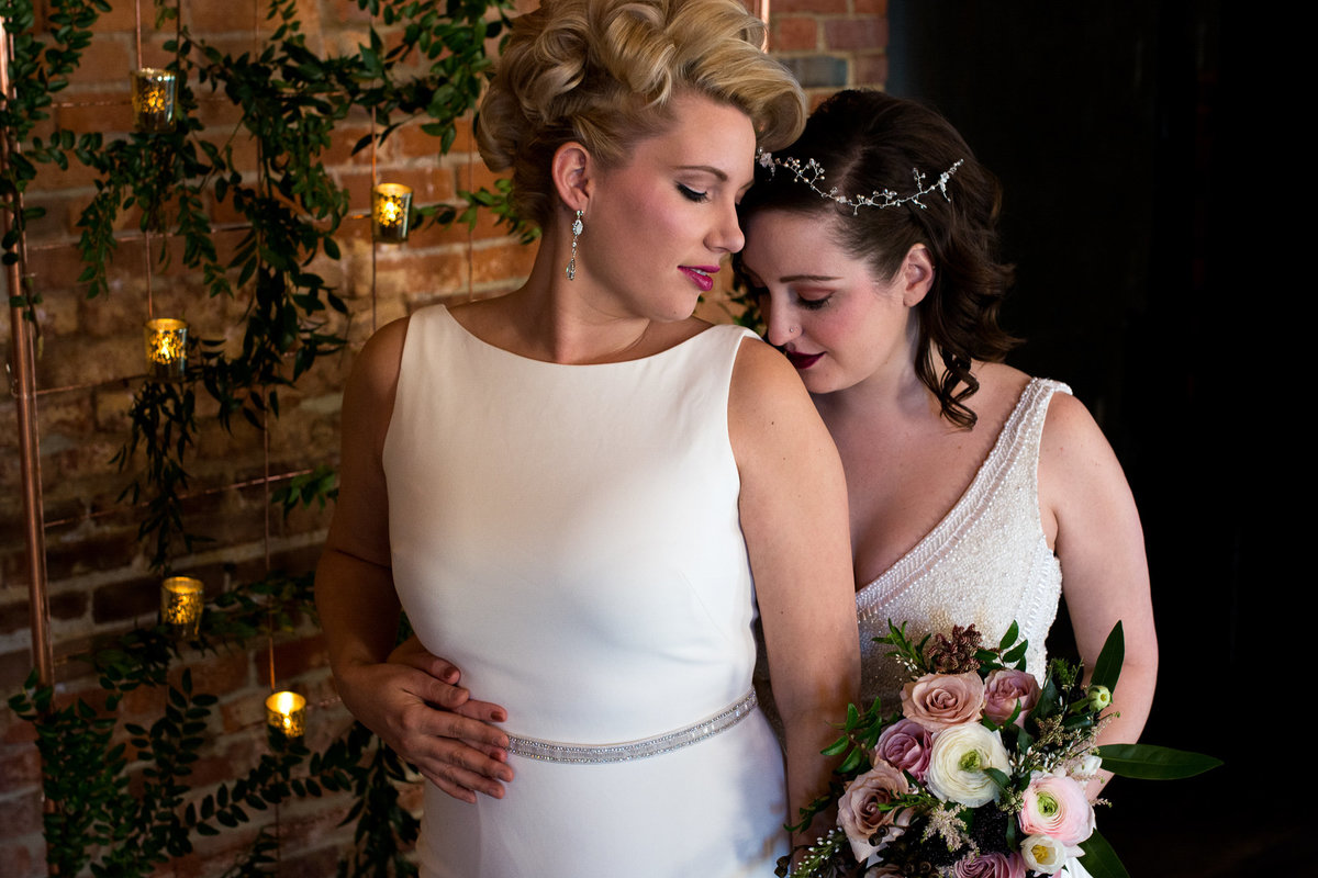 Brides snuggle together during portraits at same sex styled shoot at Highline Car House