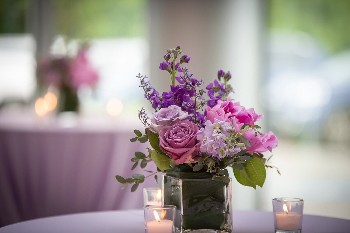 Purple cocktail tables with square glass vases filled with purple roses, pink roses purple flowers and ivory hydrangea surrounded by votive candles at a Nashville Jewish wedding at The Liff Center.