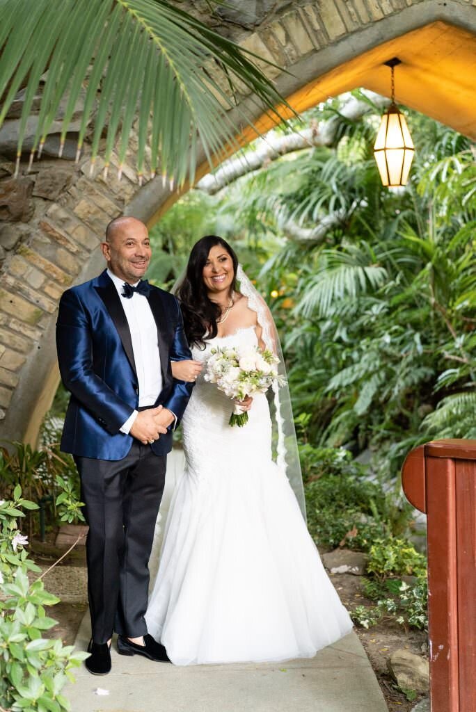 A bride smiling with her arm looped through her dads