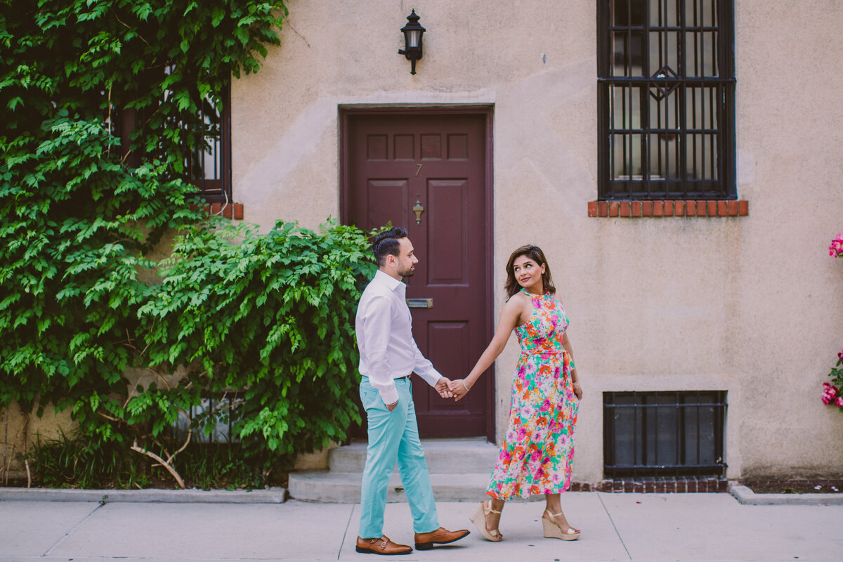 A couple walking during their engagement session in front of a european door at washington mews in nyc