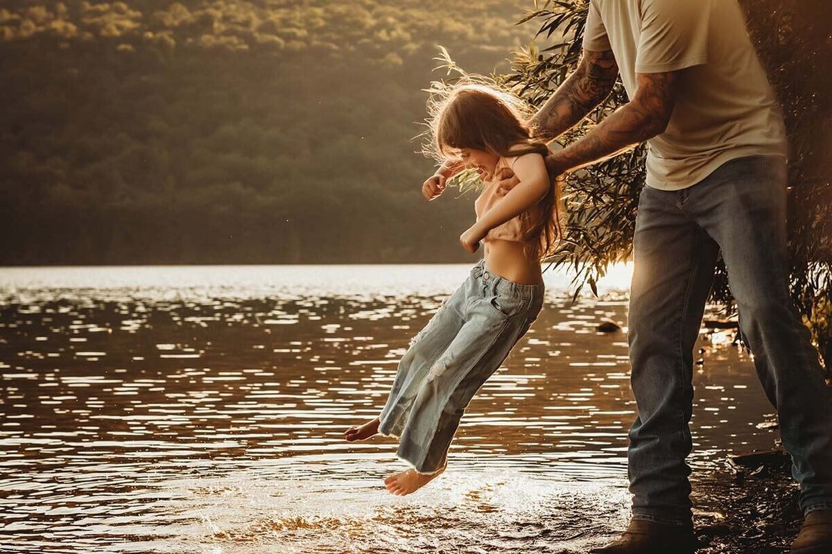 A dad swinging his daughter over the water at the lake while dragging her toes in the water while she laughs in the sunset