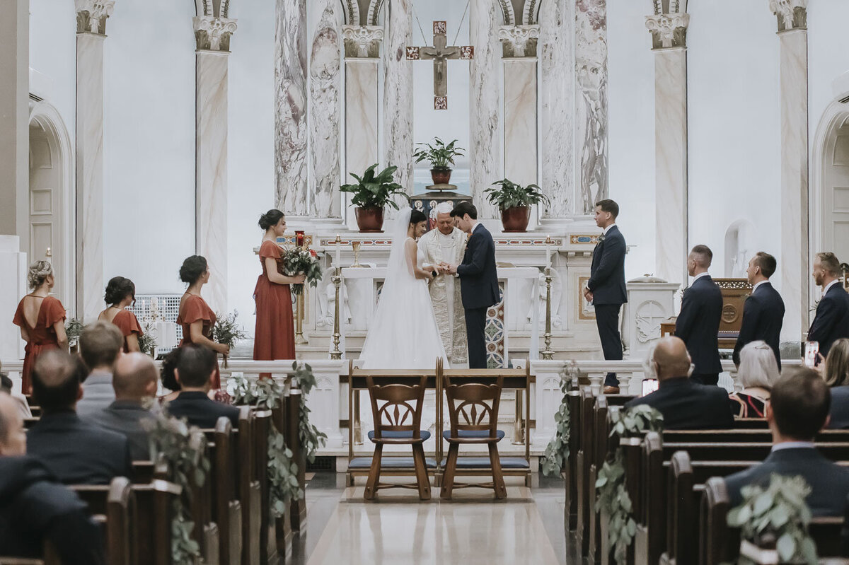 bride and groom holding hands while praying with priest