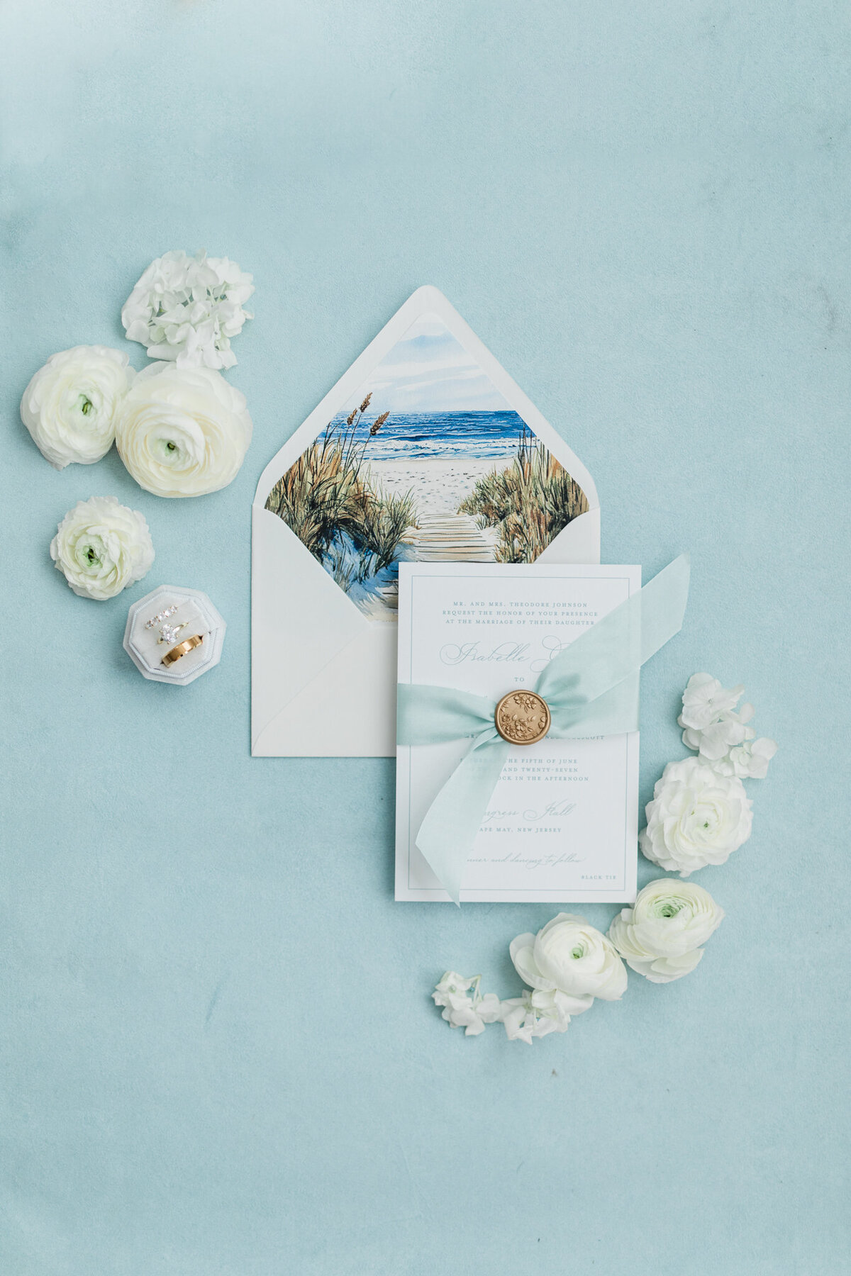 Wedding invitation suite with beach theme on light blue background and white florals