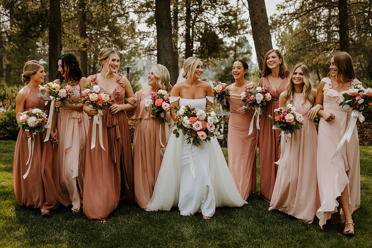 Bride with bridesmaids in terracotta dresses holding flowers in peach, coral and mauve near Sunriver Oregon